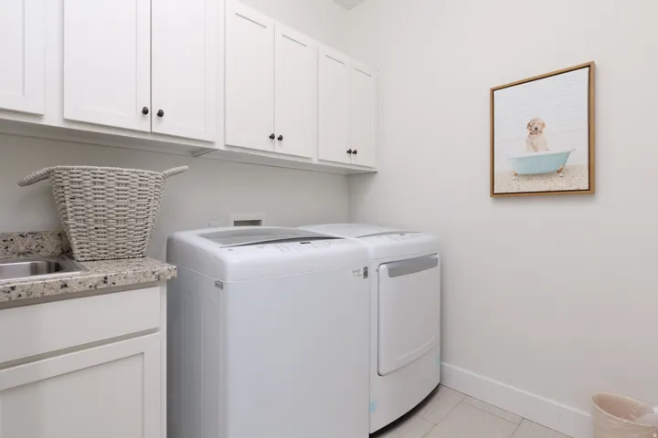Utility room featuring abundant white cabinetry with dark hardware, a countertop with an integrated sink, and light-toned flooring