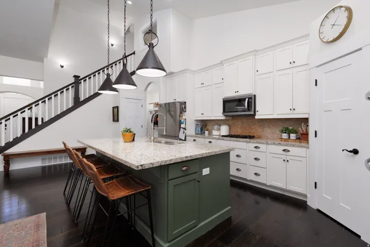 Open-concept kitchen featuring an oversized island with a light-toned countertop, white cabinetry with dark hardware, a stainless steel microwave, and dark wood-finish flooring