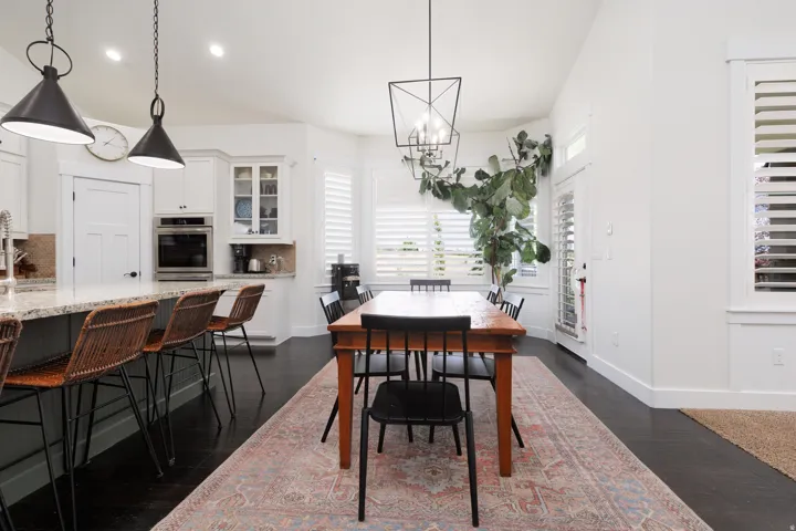 Open-concept dining area featuring dark wood-finish flooring, white walls, and a contemporary linear chandelier