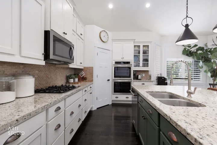 Kitchen featuring white shaker-style cabinetry, double wall ovens, a gas cooktop, a built-in microwave, and a large central island with a double basin sink and a pull-down faucet