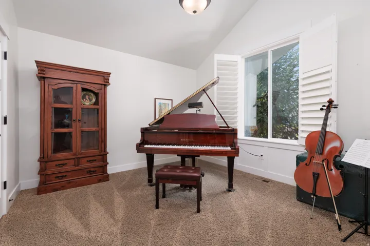 Vaulted ceiling room featuring carpet flooring and a large window with white plantation shutters