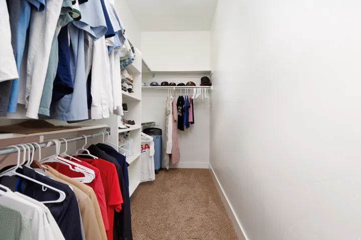 Walk-in closet featuring white built-in shelving, multiple hanging rods, and neutral carpet flooring