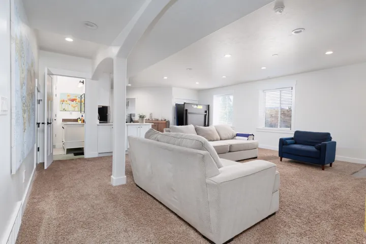Spacious carpeted living area featuring recessed lighting, a built-in wet bar with white cabinetry, and multiple windows with blinds