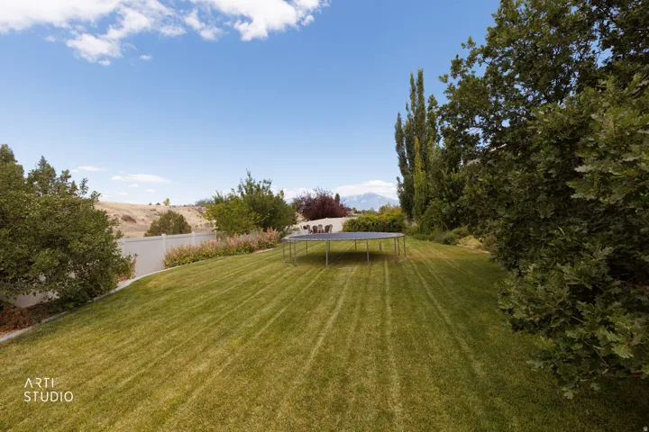 Expansive green lawn with mature trees and a white privacy fence