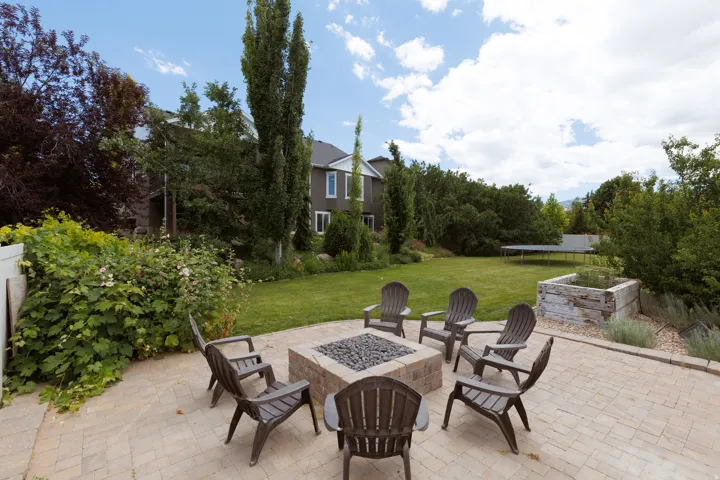 Paver patio featuring a built-in stone fire pit, surrounded by lush landscaping and a manicured lawn