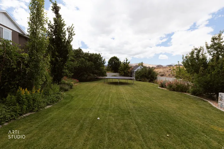 Expansive green lawn surrounded by mature trees, landscaping, and a partial privacy fence