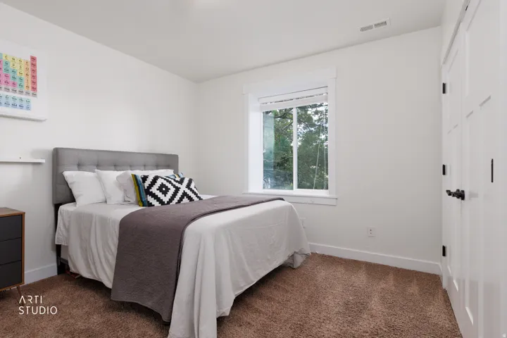 Bright bedroom featuring a large window, plush carpet, white walls, and a contemporary paneled door with matte black hardware