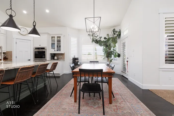 Open-concept kitchen and dining area featuring dark wood-finish flooring, white cabinetry, and granite countertops