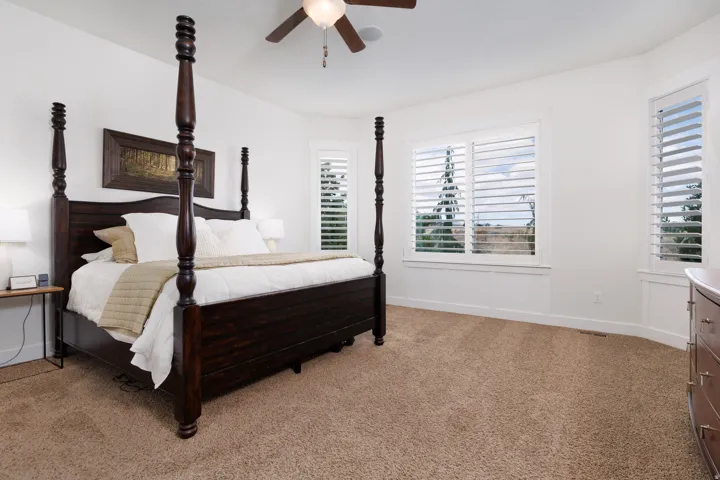 Spacious room featuring neutral carpeting, white walls, multiple windows with plantation shutters, and a ceiling fan with integrated lighting