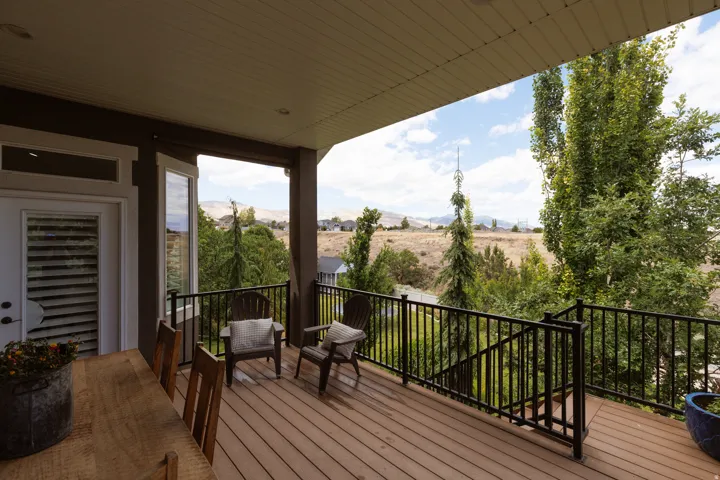 Covered composite deck featuring a slatted ceiling, black metal railings, and a hillside backdrop