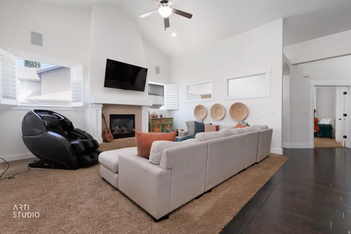 Spacious living area featuring a vaulted ceiling with a ceiling fan, a fireplace with a mantel, plantation shutters, and dark wood-finish flooring