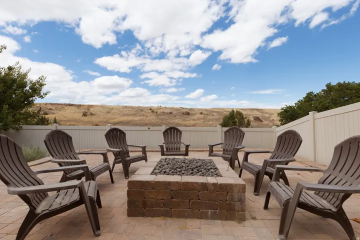 Paved patio featuring a built-in brick fire pit, surrounded by a privacy fence, and backed by natural terrain