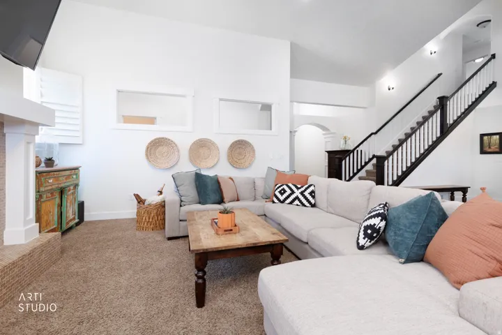 Spacious living area featuring carpet flooring, crisp white walls, and a prominent staircase with dark wood newel posts and white balusters