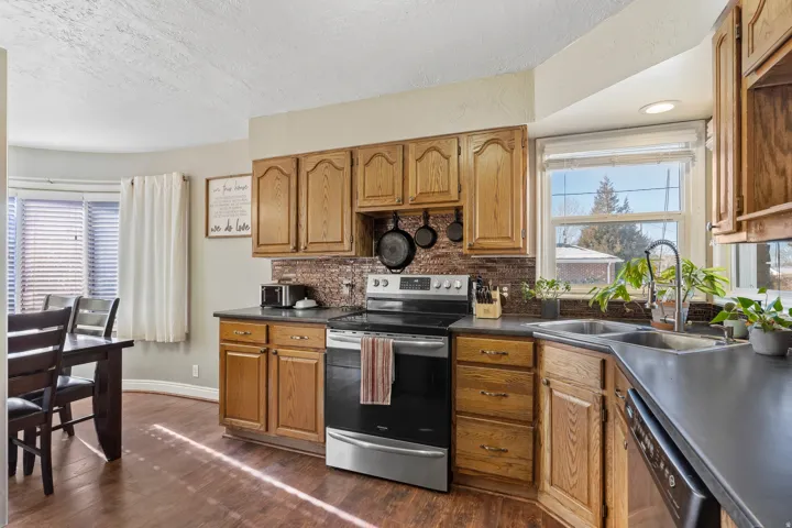 Kitchen featuring wood-finish flooring, oak cabinetry, dark countertops, a mosaic tile backsplash, and a stainless steel oven/range