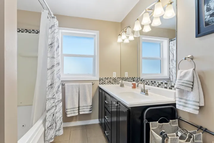 Bathroom featuring a double vanity with two sinks, dark cabinetry, and a full-width mirror