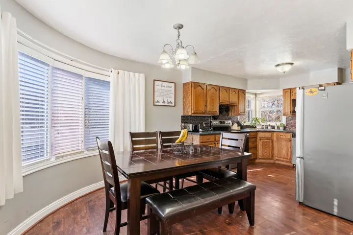 Dining area featuring a curved bay window with blinds, wood-finish flooring, and a chandelier-style ceiling fixture