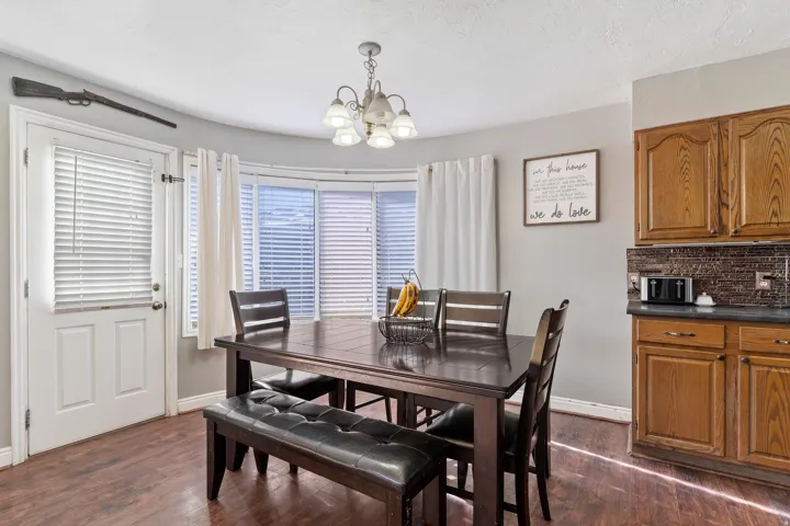 Dining area featuring wood-finish flooring, a bay window with blinds, and a built-in kitchen cabinet with a tile backsplash