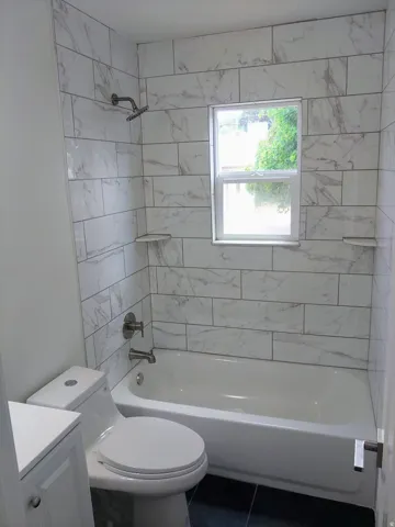 Bathroom featuring a white subway tile shower surround with integrated shelves, a white bathtub, and a modern toilet