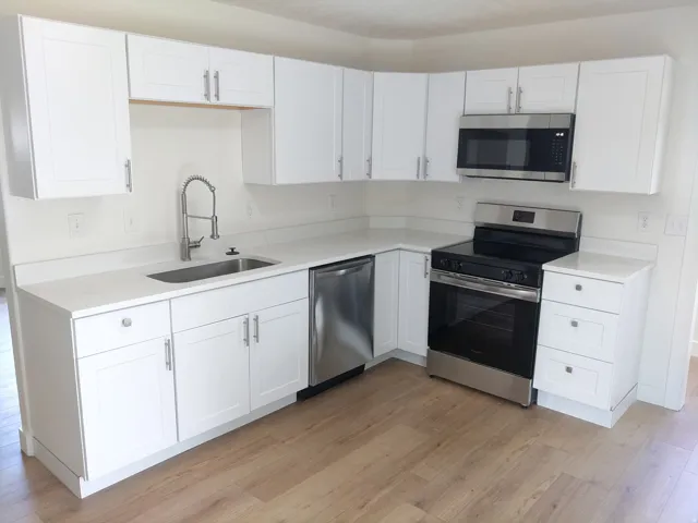 Modern kitchen featuring white shaker cabinetry, stainless steel appliances, light-toned wood-finish flooring, a stainless steel sink with a high-arc faucet, and light countertops