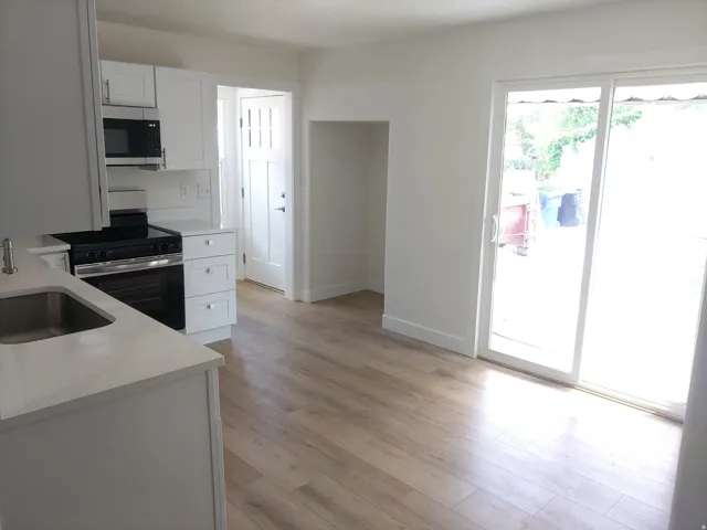 Open-concept kitchen area featuring light wood-finish flooring, white cabinetry, integrated microwave, and a stainless steel sink