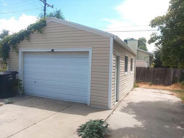 Detached garage with horizontal siding, a roll-up garage door, and a side entry door