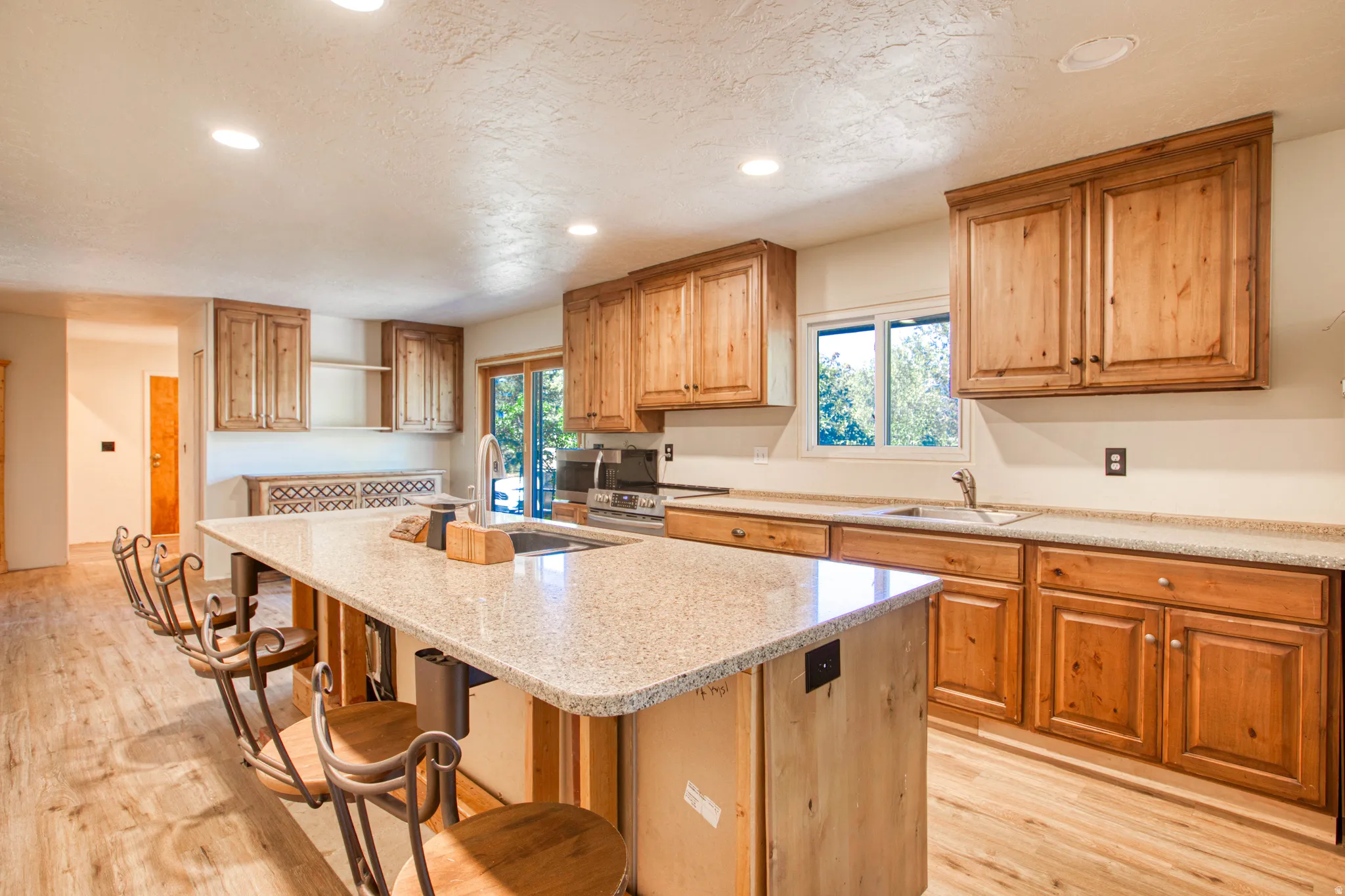 Kitchen featuring an expansive island with a stone-finish countertop, wood-finish flooring, recessed lighting, wood cabinetry, and a stainless steel sink