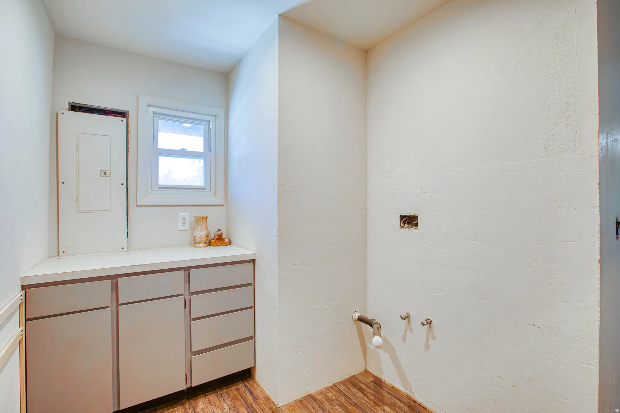 Utility area featuring wood-finish flooring, built-in cabinetry with a light-toned countertop, a single window, and visible plumbing hookups
