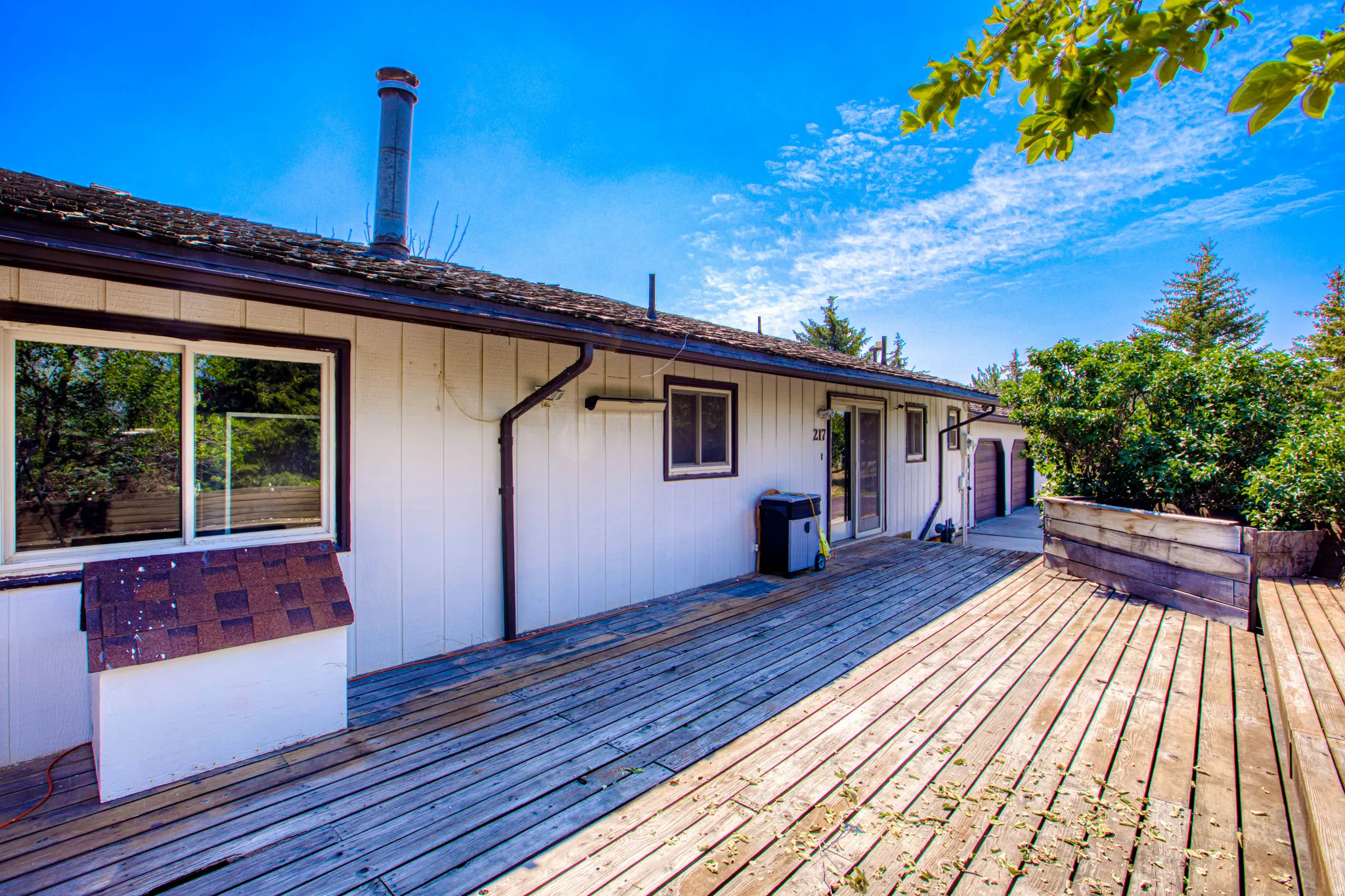 Expansive wooden deck with planter boxes, white vertical siding, and a brown shingle roof