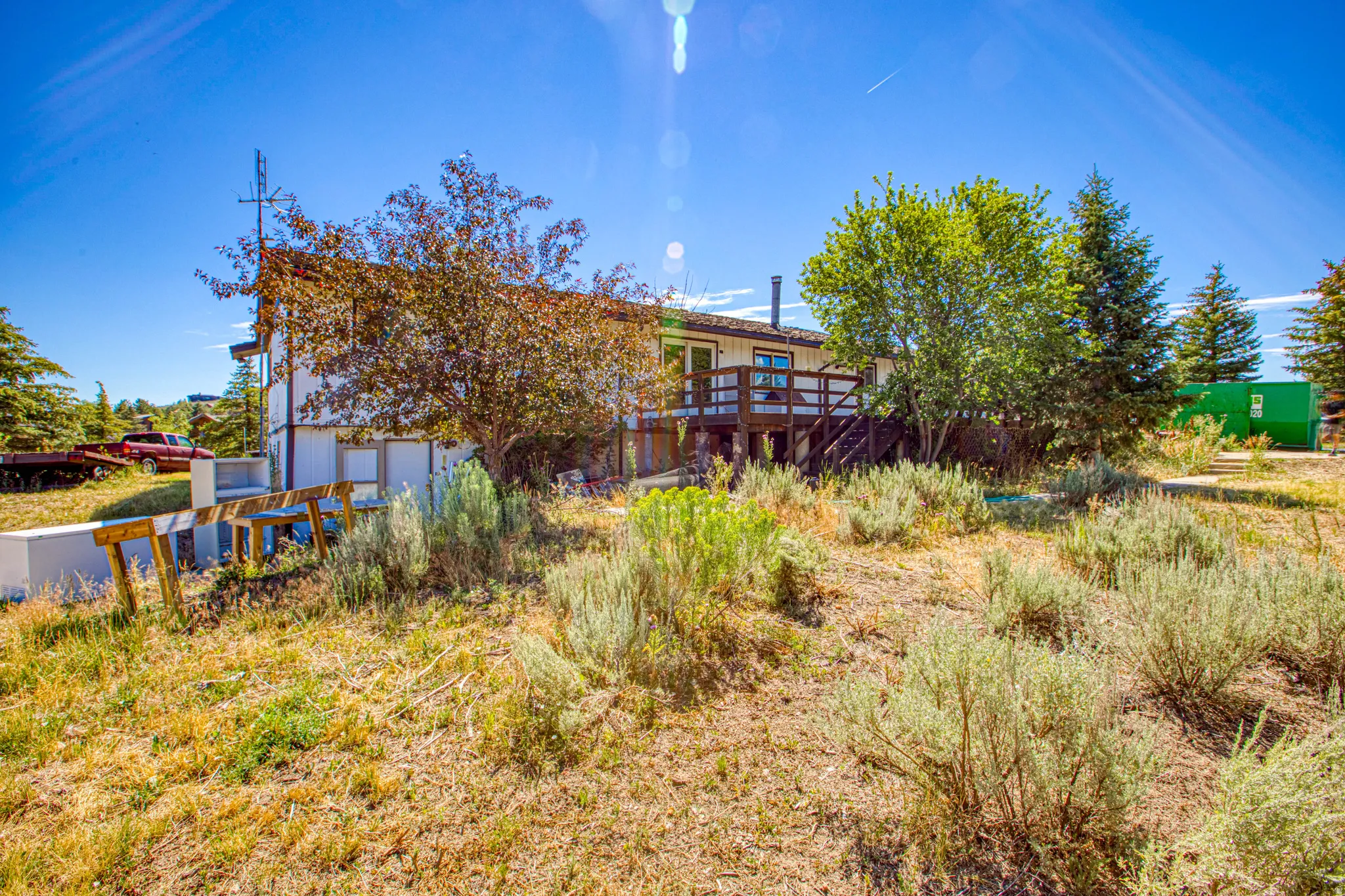 Contemporary home exterior featuring a multi-level deck, white siding, and a sloped, natural landscape with established trees and shrubs