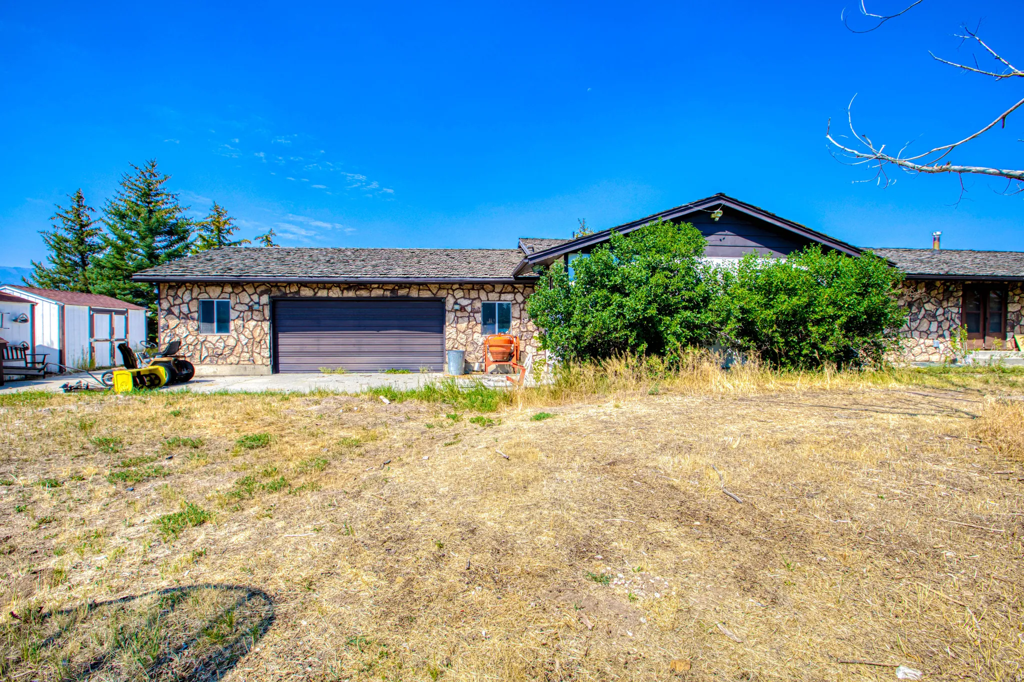 Stone exterior, attached garage, gabled roofline, multiple windows, additional shed structure