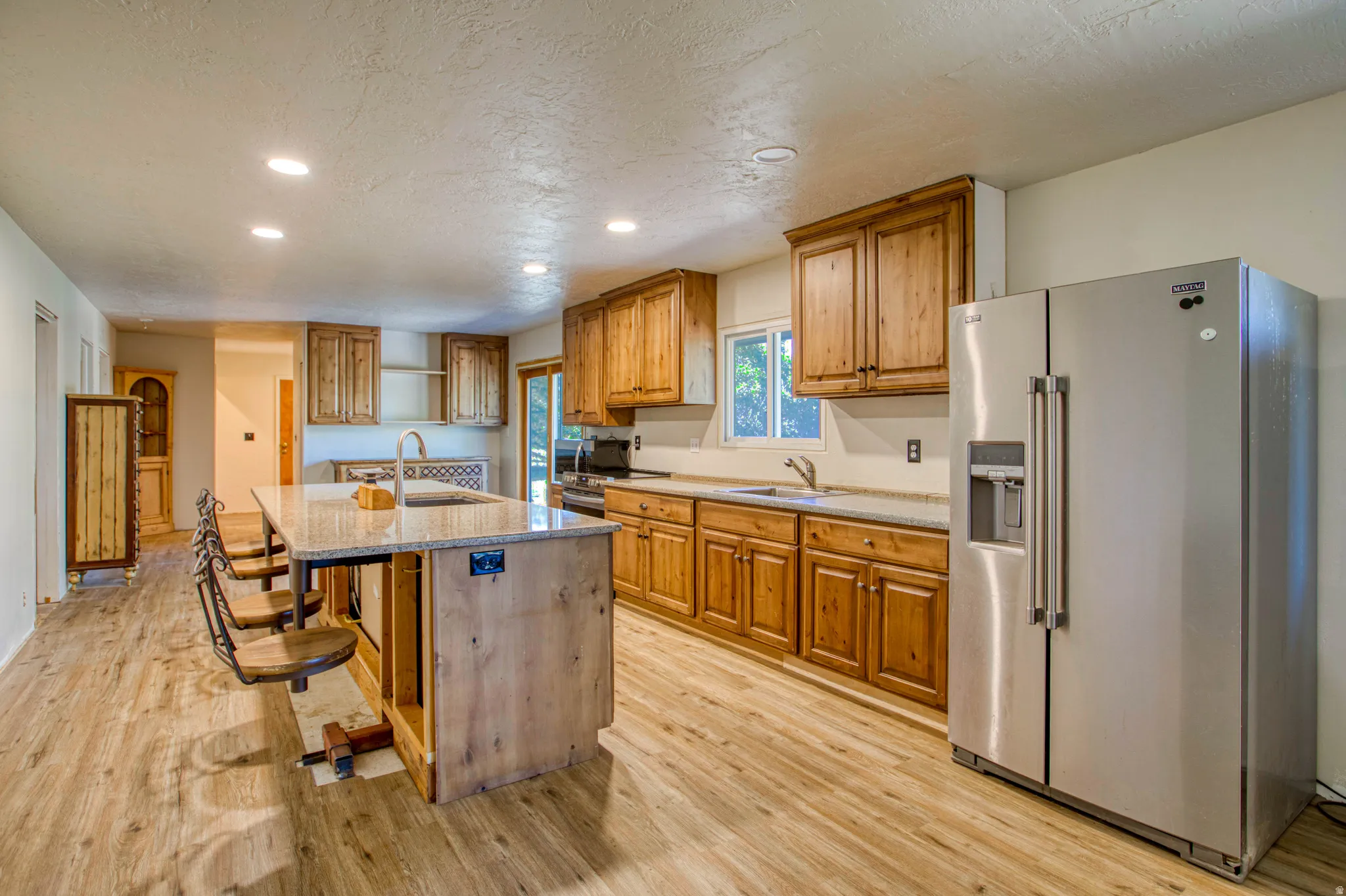 Kitchen featuring a central island with bar seating, wood-finish flooring, recessed lighting, wood cabinetry, and a side-by-side stainless steel refrigerator