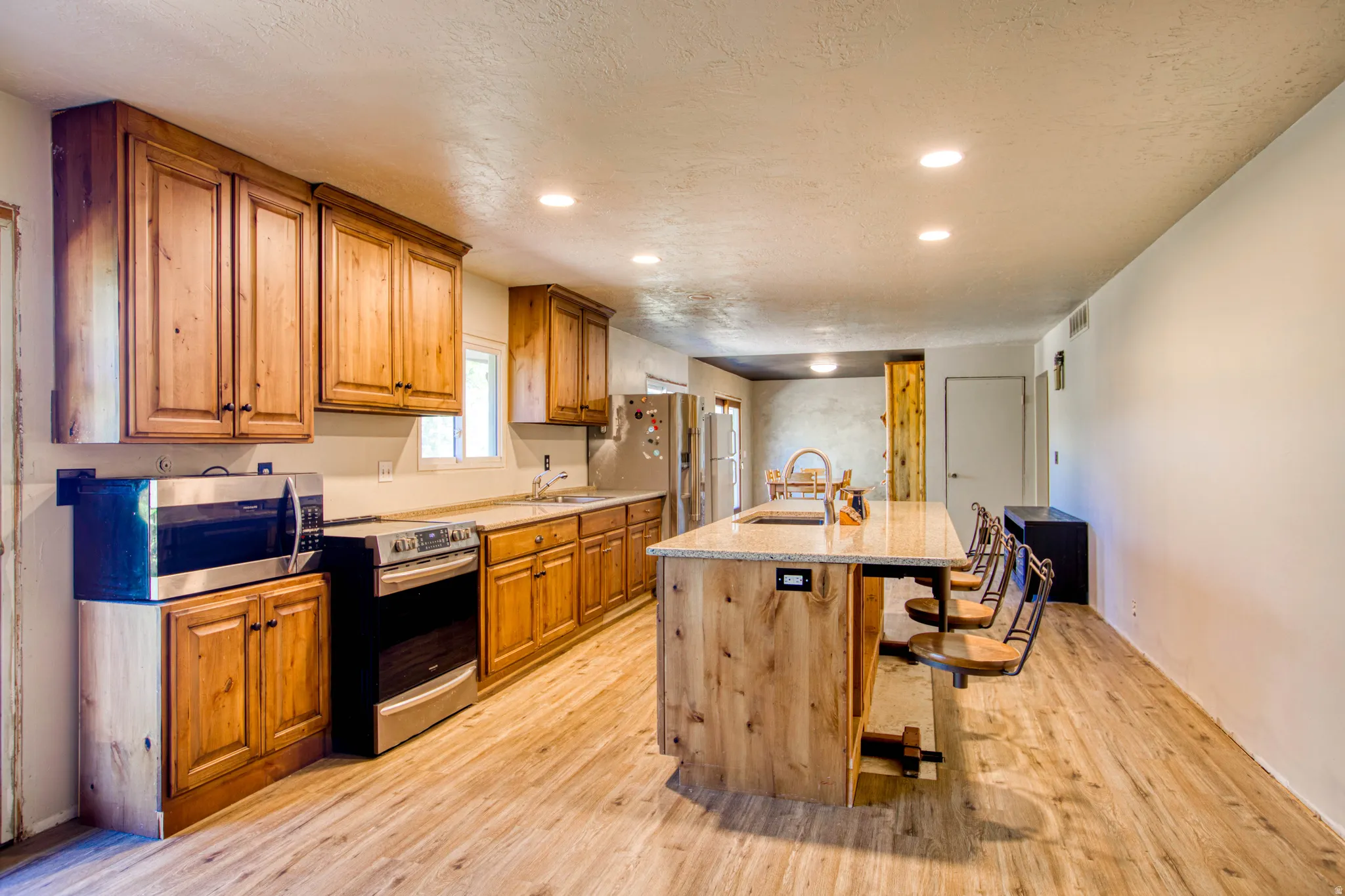 Expansive kitchen featuring wood-finish flooring, recessed lighting, wood cabinetry, a center island with countertop seating, and stainless steel appliances