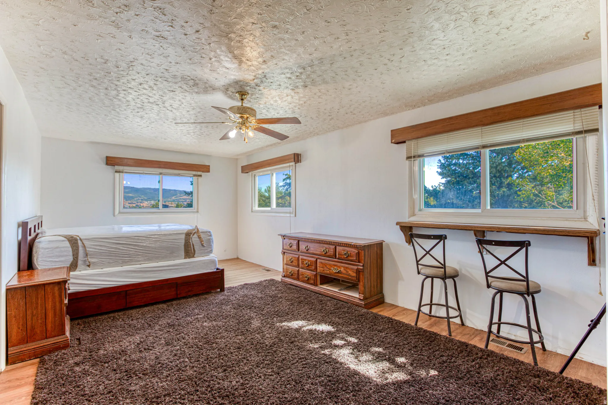 Spacious room featuring wood-finish flooring, a ceiling fan, and multiple windows with outdoor scenery