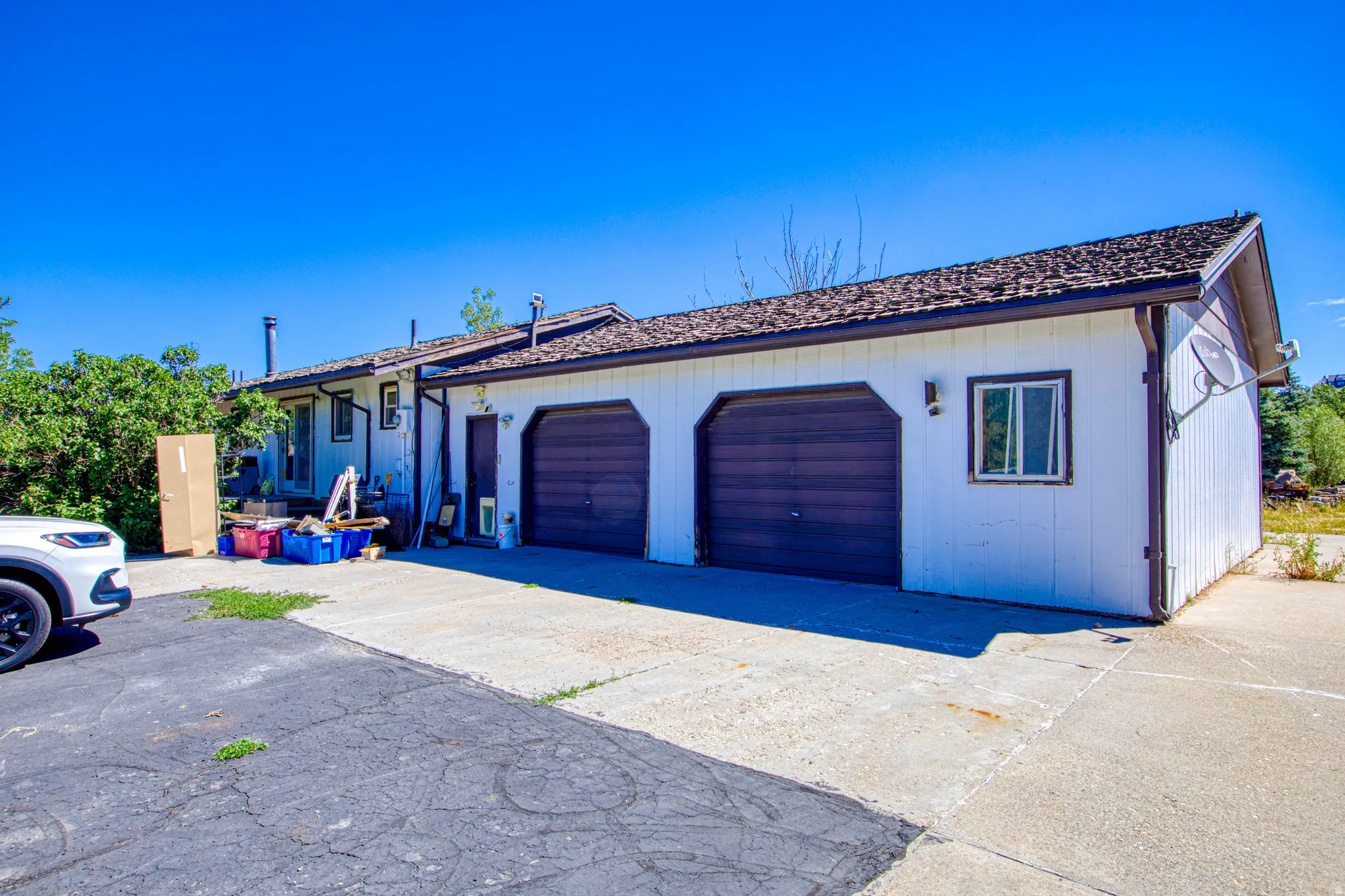 Exterior featuring a two-car garage with arched dark wood-finish doors, white siding, and a shingled roof