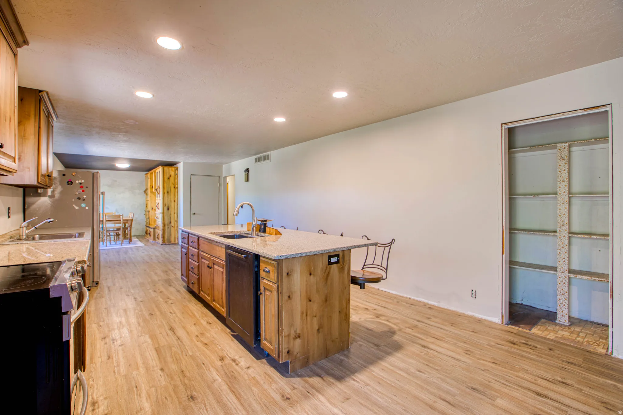 Kitchen featuring wood-finish flooring, recessed lighting, and a large central island with a light-toned countertop and integrated sink