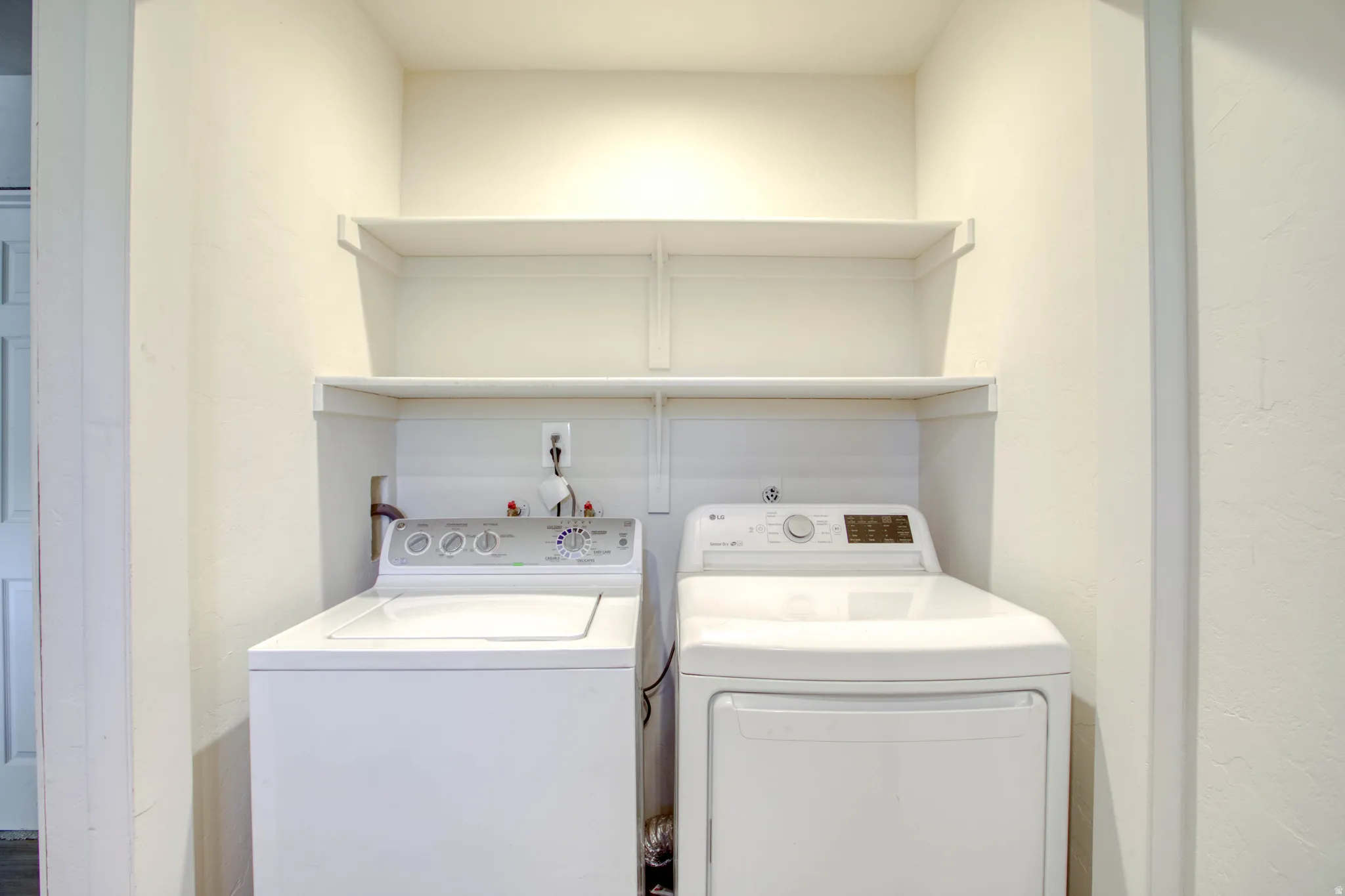 Dedicated laundry area featuring a top-load washing machine, front-load dryer, and integrated wall shelving