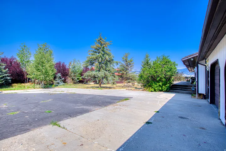Expansive concrete and asphalt driveway with mature trees and a multi-level wood deck