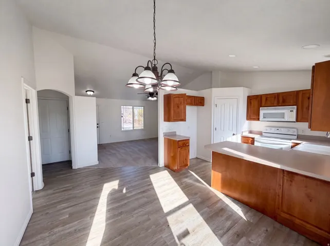 Open-concept kitchen and dining area featuring wood-finish flooring, vaulted ceilings, and a bronze-finish chandelier