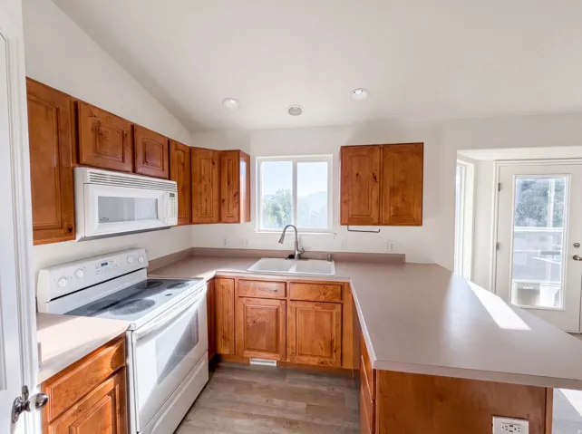 Kitchen featuring wood-finish cabinetry, light-toned countertops, and a white appliance suite