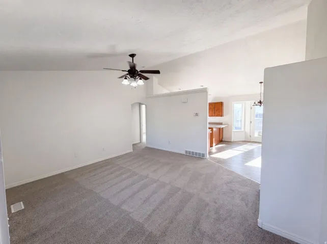 Spacious living area featuring vaulted ceilings, a ceiling fan with integrated lighting, and neutral carpeting
