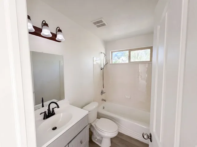 Bathroom featuring a white vanity with integrated sink, matte black faucet, and wood-finish flooring