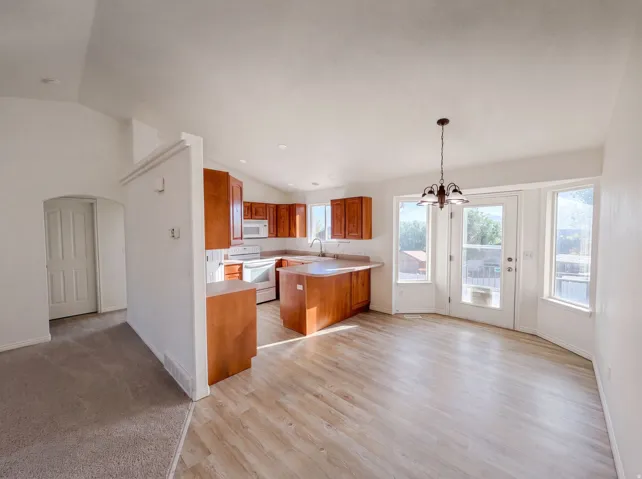 Open-concept living space featuring wood-finish flooring, vaulted ceilings, and a kitchen with warm wood cabinetry