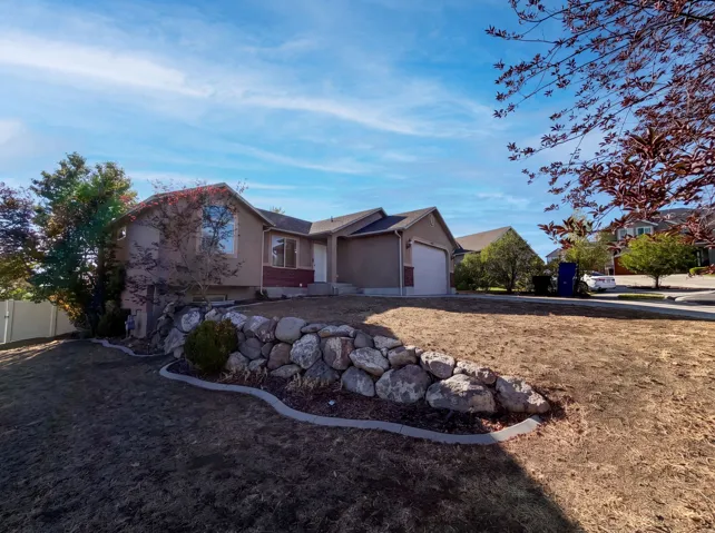 Single-story residence featuring a stucco exterior with brick accents, an integrated two-car garage, and a rock retaining wall