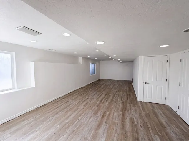 Spacious room featuring wood-finish flooring, recessed lighting, and bright white walls
