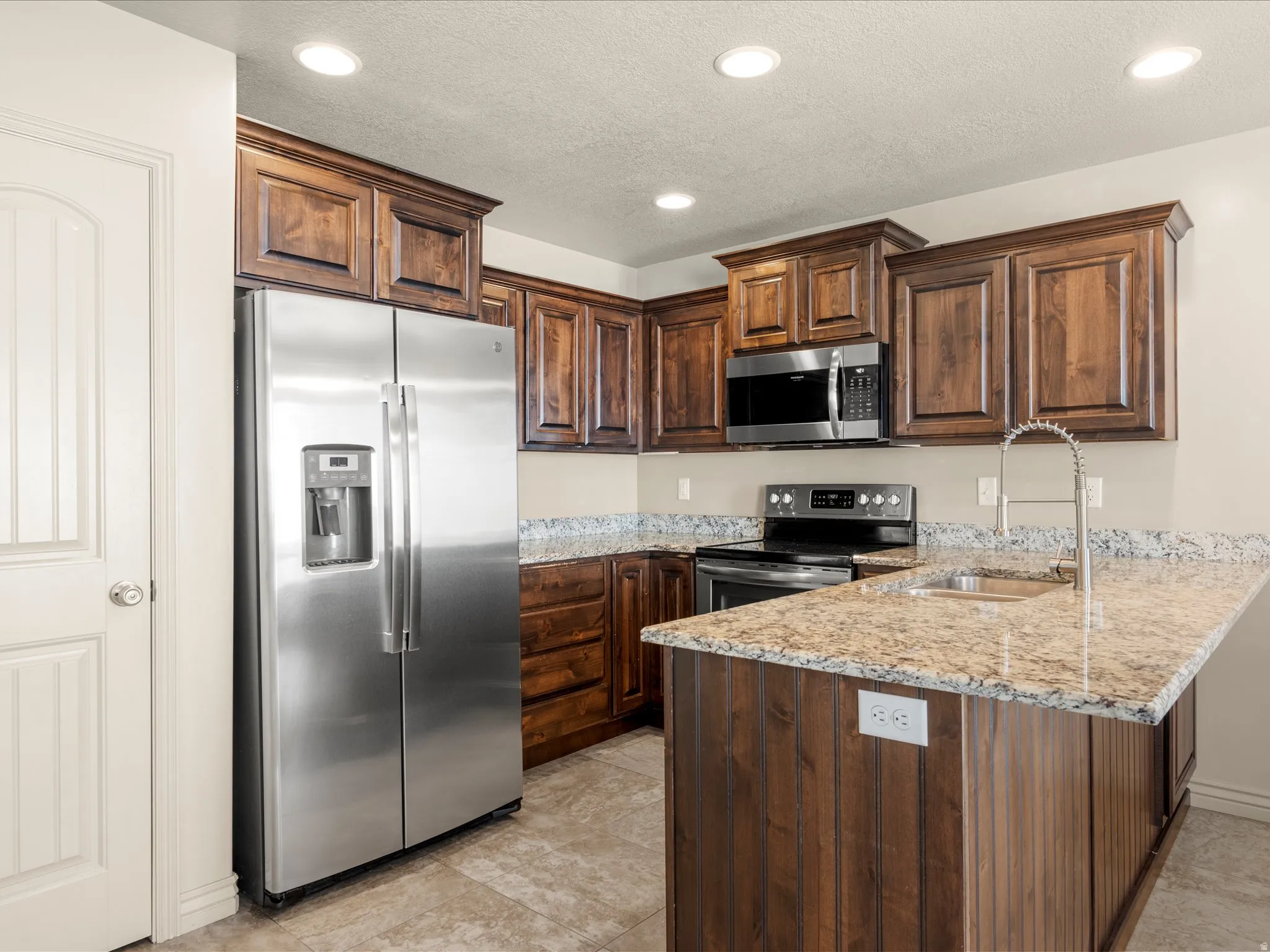 Modern kitchen featuring stainless steel appliances, dark wood-finish cabinetry, and light-toned granite countertops