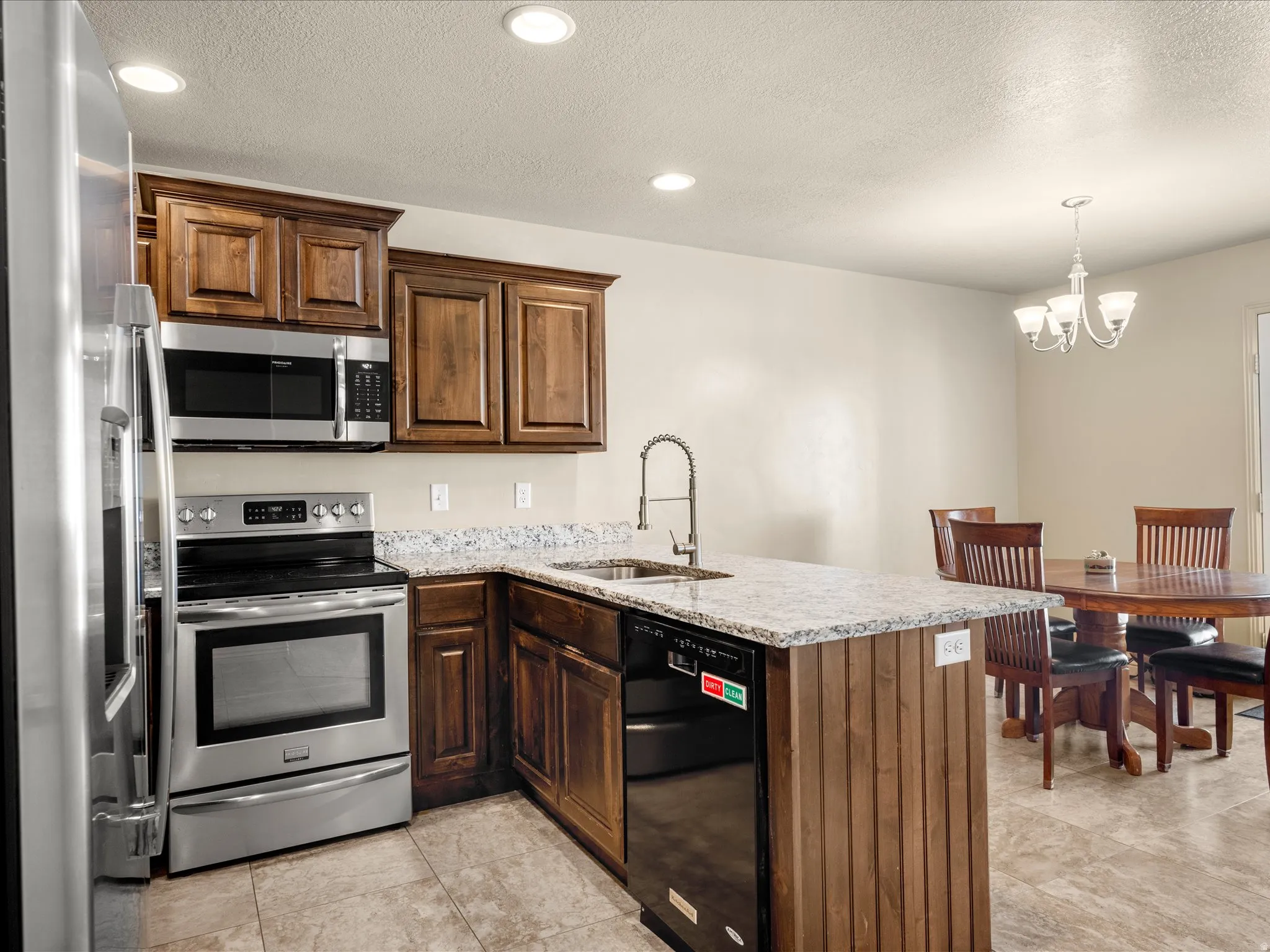 Contemporary kitchen featuring stainless steel appliances, wood cabinetry, stone countertops, and tile flooring