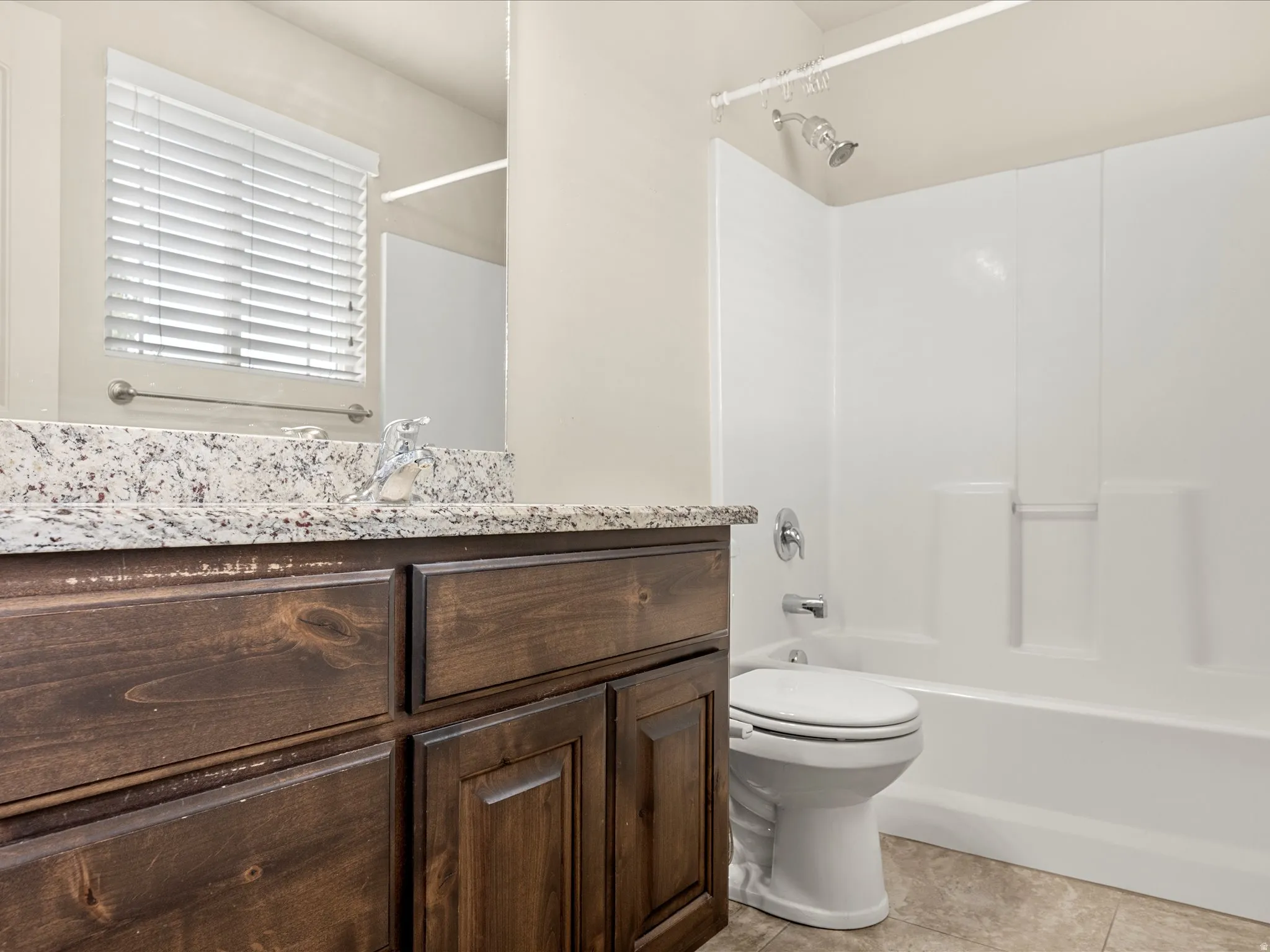 Bathroom featuring a dark wood-finish vanity with a speckled countertop, a white toilet, and a white shower-over-tub combination with chrome fixtures
