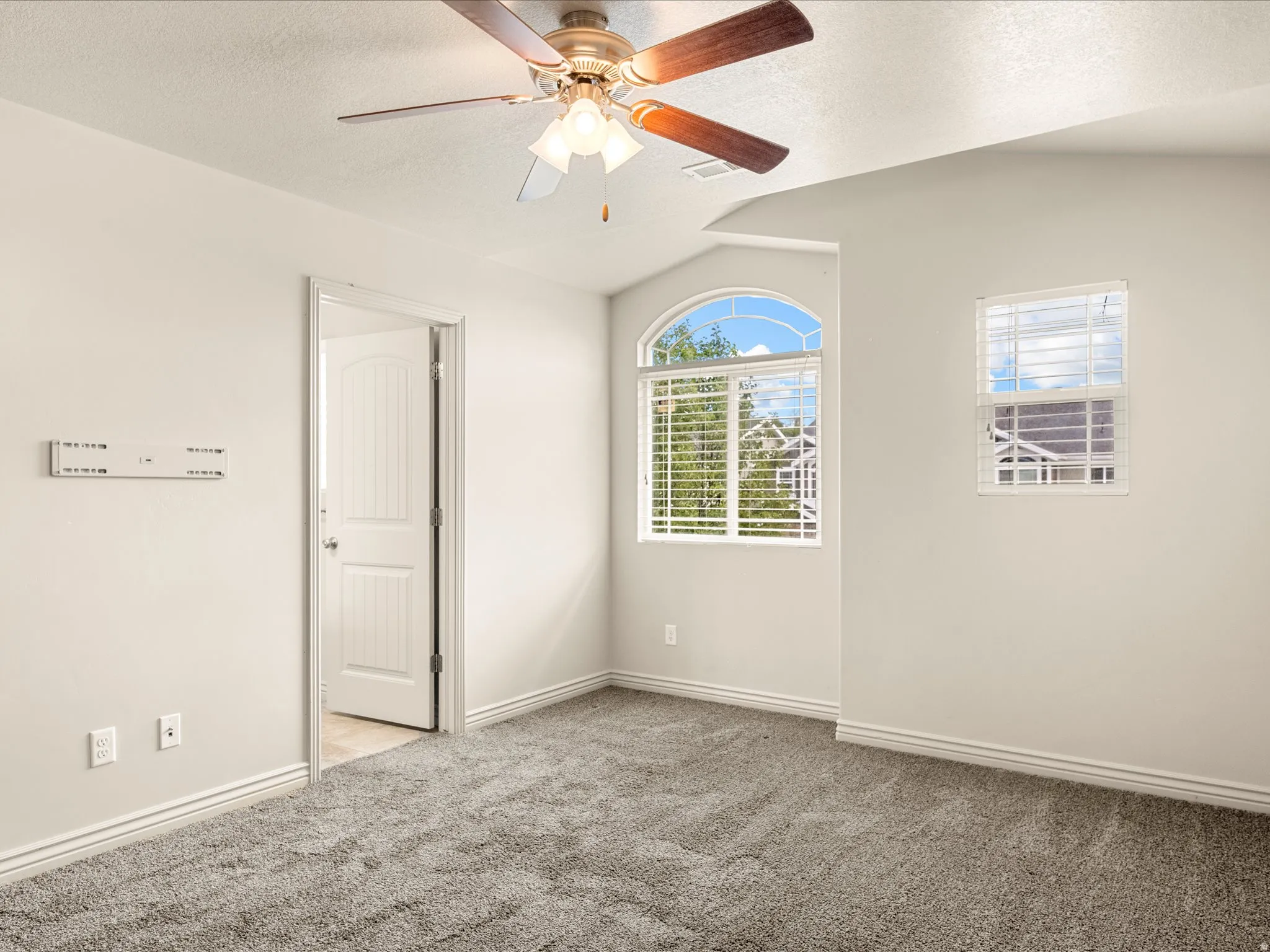 Carpeted room featuring a ceiling fan with light fixture, arched window, standard window, and white trim