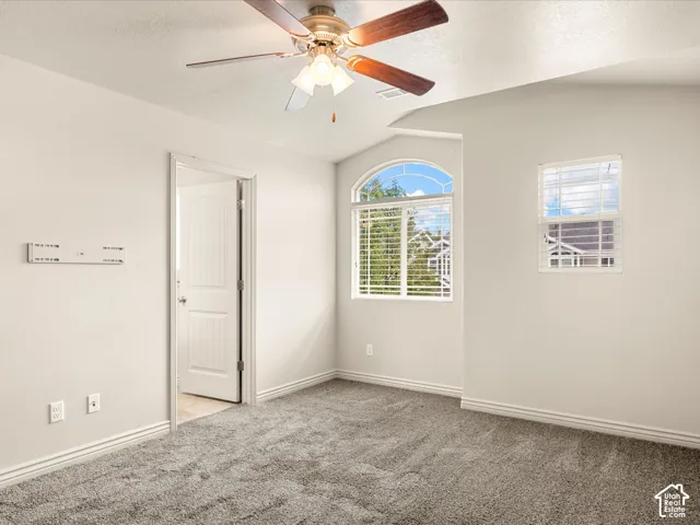 Carpeted room featuring a ceiling fan with light fixture, arched window, standard window, and white trim