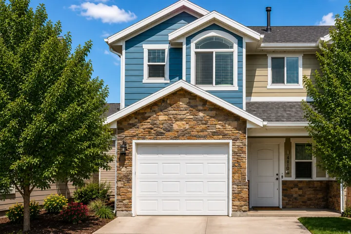 Multi-level residence featuring a stone-clad facade, attached garage, and blue siding